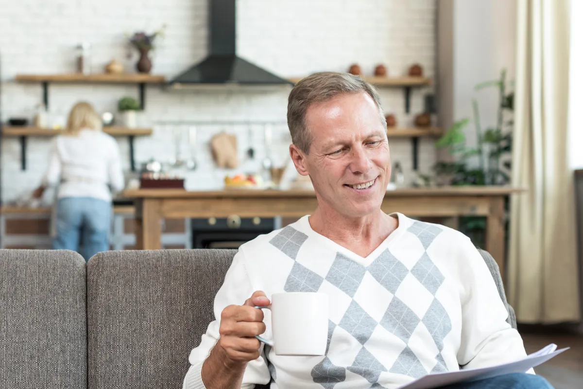 Smiling man with a coffee cup and papers on a sofa at home