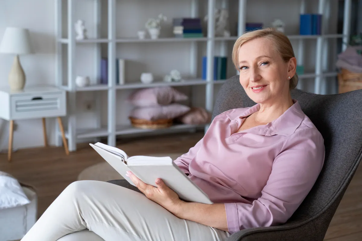 Smiling woman reading a book in an armchair at home