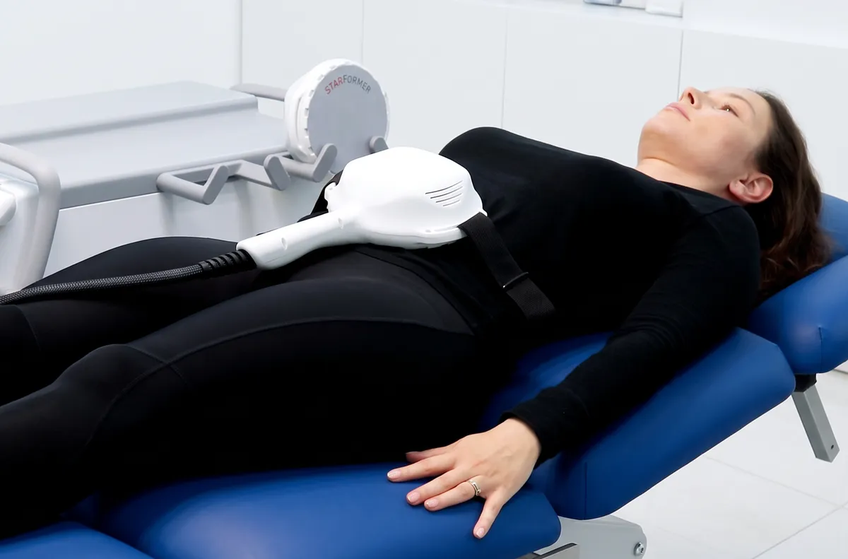 A patient, fully clothed, on a treatment bed with the StarFormer applicator strapped over her abdomen