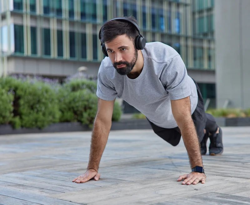 A man wearing headphones holding a plank on an outdoor deck
